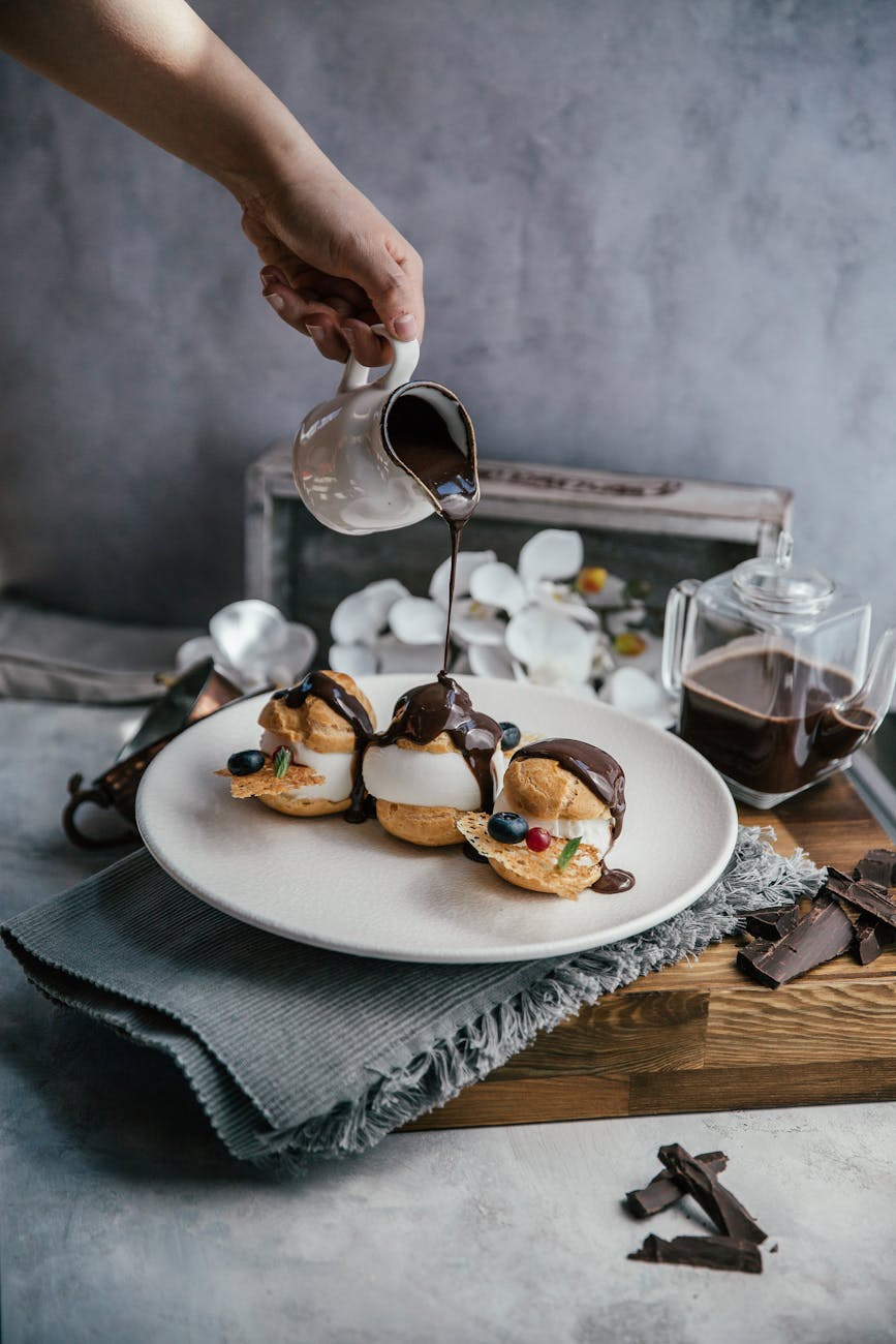 person pouring chocolate on profiteroles